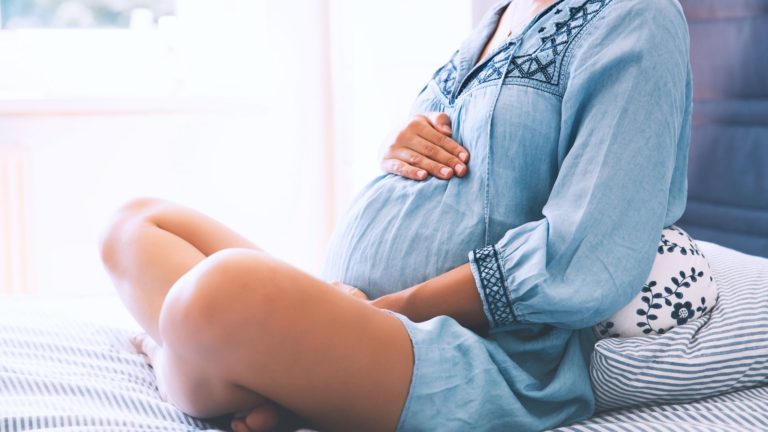 pregnant woman in blue dress sitting on a bed