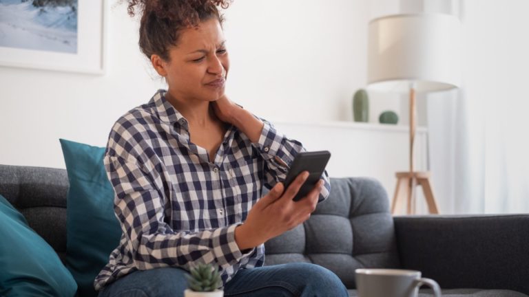 black woman with sore neck looking at cell phone