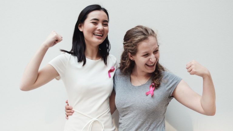 two women flexing and wearing pink ribbons for breast cancer awareness