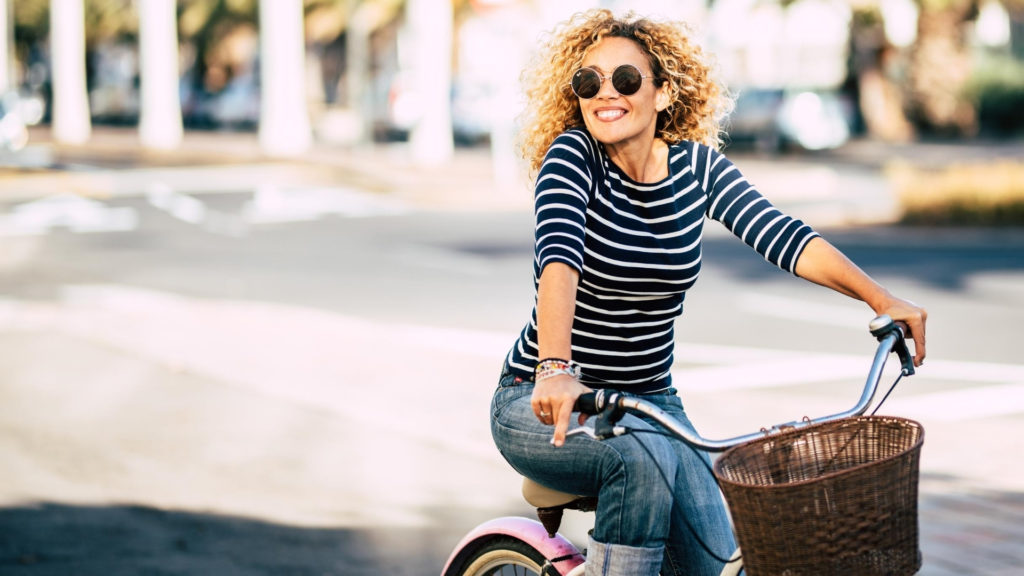 woman with curly hair riding a bike while wearing sunglasses