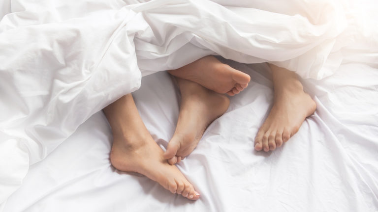 couple's feet underneath a bed sheet