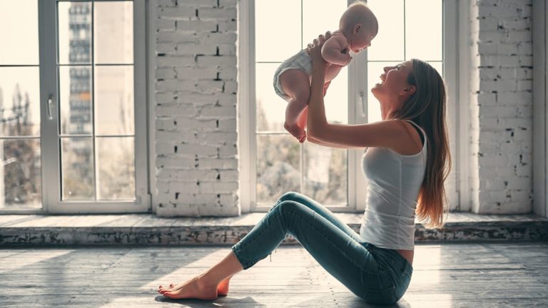 moom holding baby in the ai while sitting on the ground