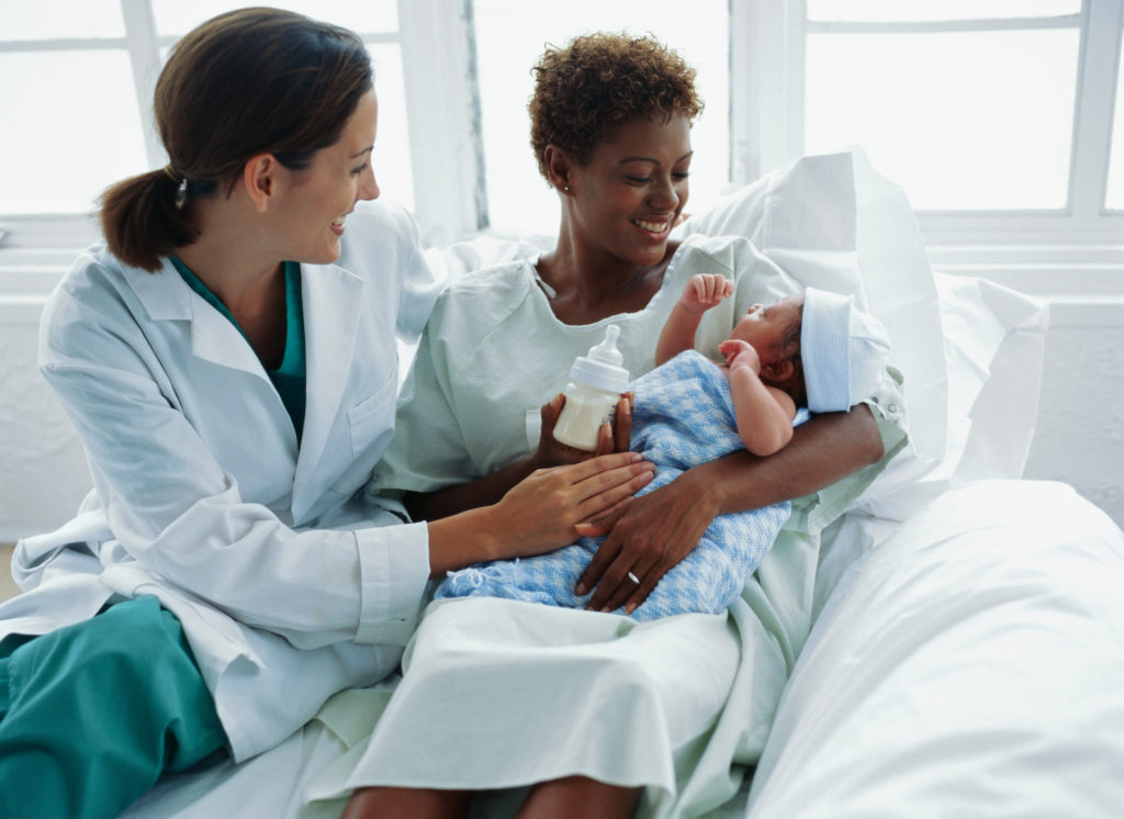 view of a doctor watching a new mother feed the baby with a bottle