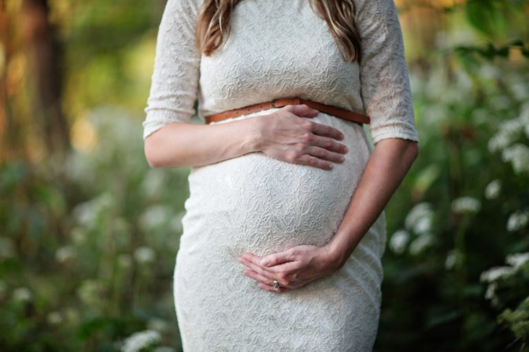 pregnant woman in white dress holding her belly in a park
