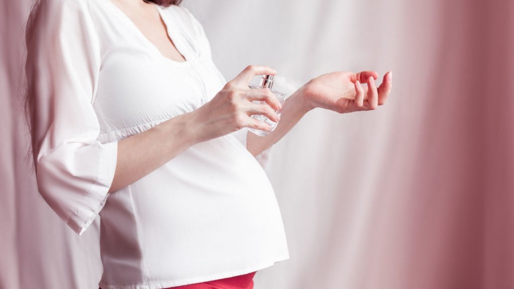 pregnant woman spraying perfume on her hand