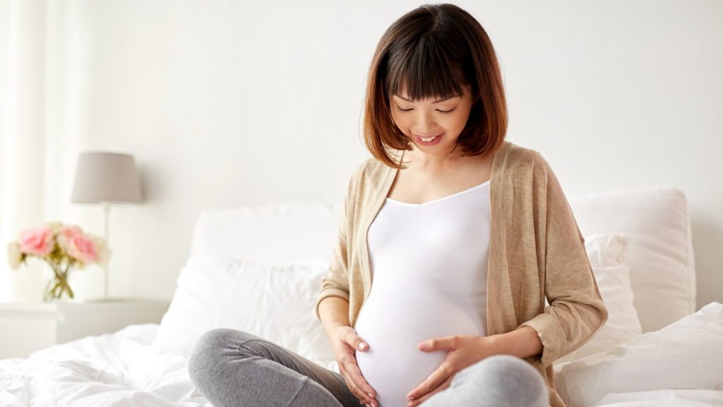 pregnant woman holding her belly and sitting on a bed